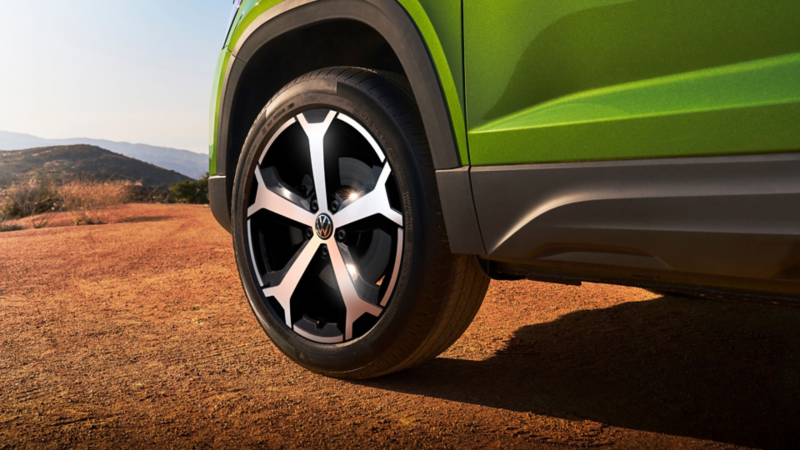 Close view of the available 19" wheels on a Taos shown in Bright Moss Green with mountains in the background.