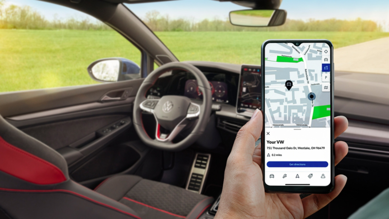 Frontal view of the Lapiz Blue Metallic Golf R driving on a racing track with bleachers in the background. 