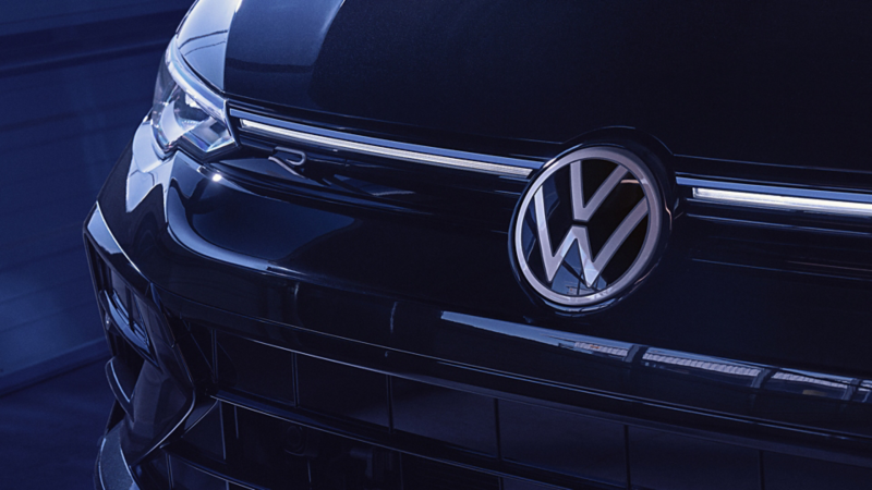 Close-up of the front grille and badge of a Volkswagen Golf R in Mythos Black Metallic under blue lighting.
