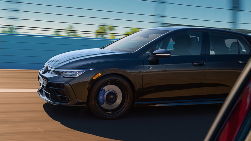 Side view of a Volkswagen Golf R in Mythos Black Metallic driving on a racetrack, captured in motion with blurred background