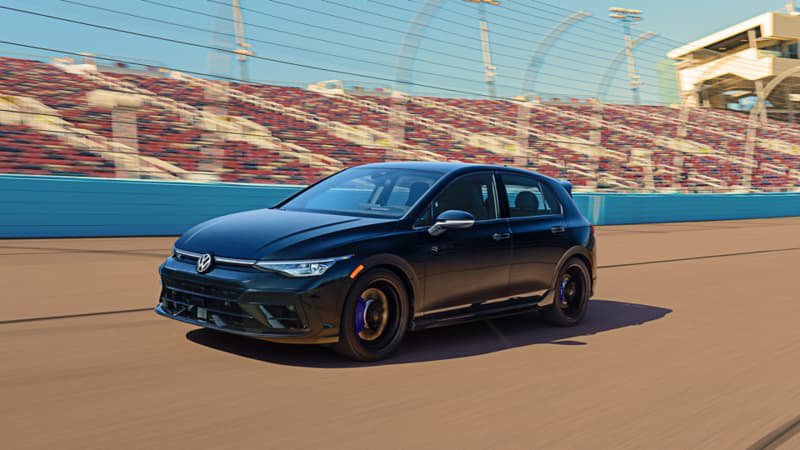 Volkswagen Golf R in Mythos Black Metallic driving on a racetrack with grandstands in the background.