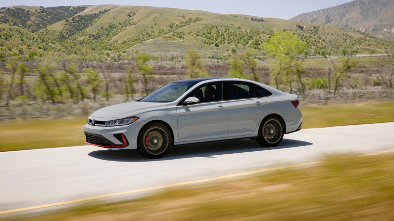 Side view of a Jetta GLI shown in Monument Gray driving with mountains in the background.