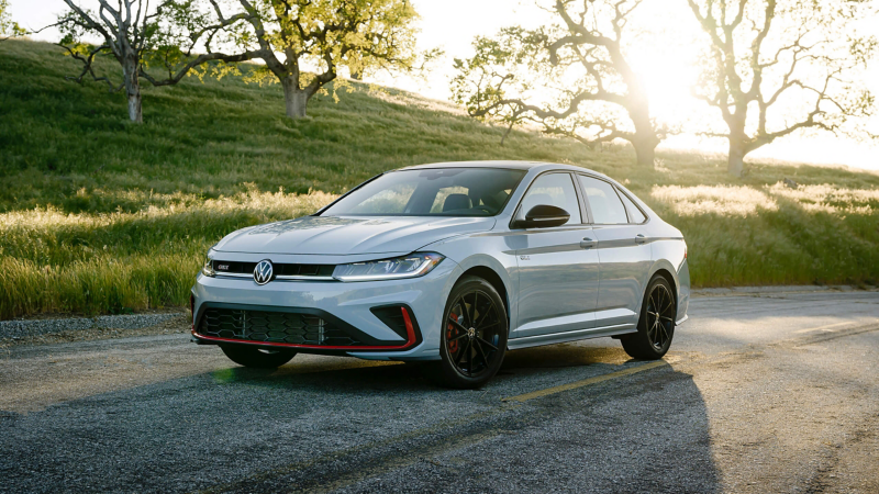 Front 3/4 view of a Jetta GLI shown in Monument Gray parked with a green hill with trees in the background