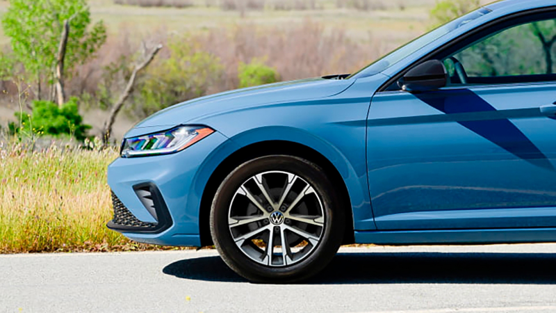 Profile view of a parked Jetta shown in Monterey Blue Pearl highlighting the driver side front wheel with trees in the background