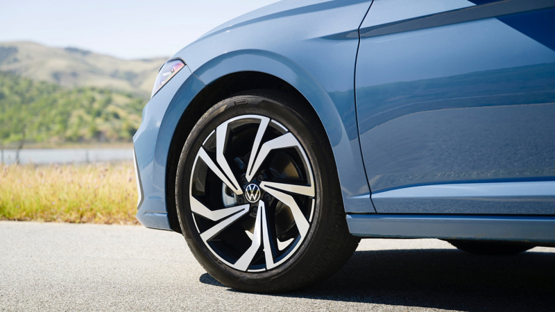Close up view of available 17” alloy wheels on a Jetta shown in Monterey Blue Pearl parked with wooded hills in the background