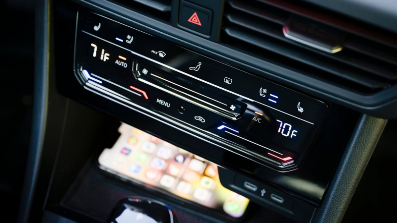 Controles de aire acondicionado del Jetta con un teléfono cargándose en la base de carga disponible en la consola central para dispositivos compatibles