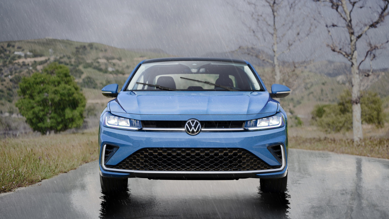 Head-on view a Jetta shown in Monterey Blue Pearl parked in rainy weather with wooded hills in the background