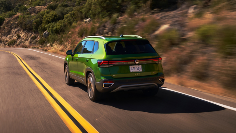 Rear view of a Taos shown in Bright Moss Green driving on a mountain road.