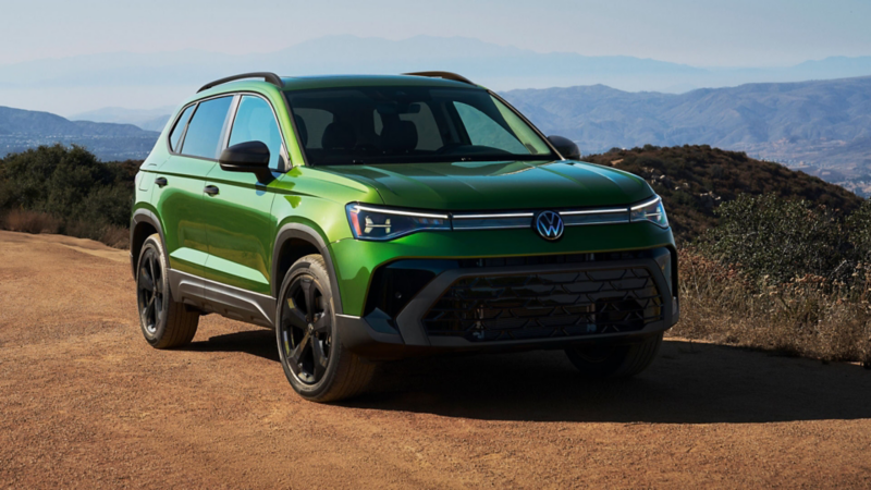 Front 3/4 view of a parked Taos SE Black Edition shown in Bright Moss Green with mountains in the background.
