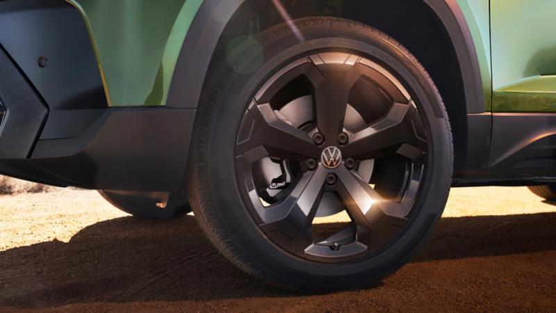 Close view of the available 19" black alloy wheels on a Taos shown in Bright Moss Green with mountains in the background.