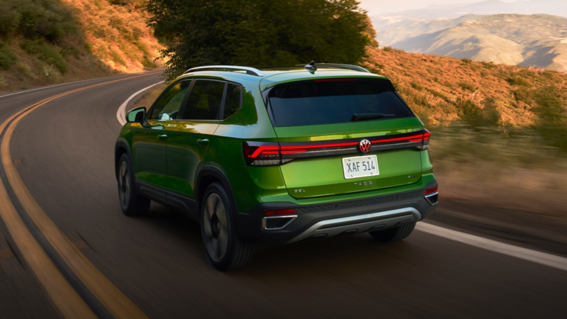 Rear view of a Taos shown in Bright Moss Green driving with mountains in the background.