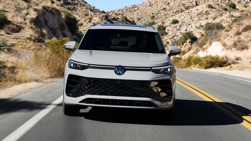 Head-on view of a Tiguan shown in Sandstone driving on a mountain road with rocks and shrubs making up the landscape.