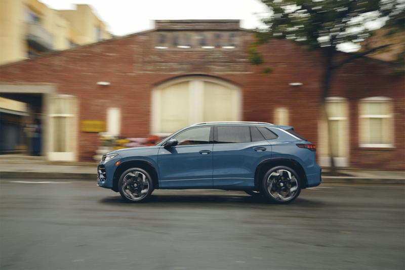 Profile view of a Tiguan shown in Monterey Blue Pearl driving past a coffee shop with a brick facade.