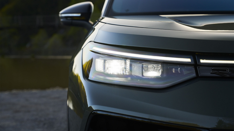 Close up view showing the LED headlights of a Tiguan at dusk shown in Avocado Green Metallic.