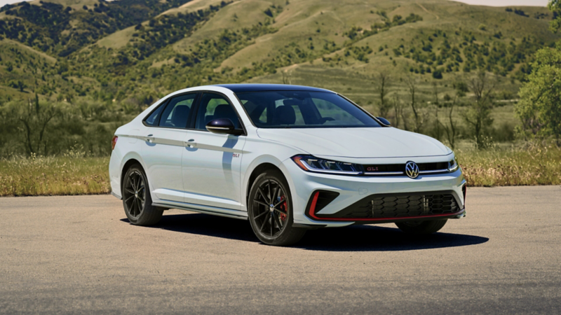 Front 3/4 view of a Jetta GLI shown in Monument Gray parked with a green hill with trees in the background.
