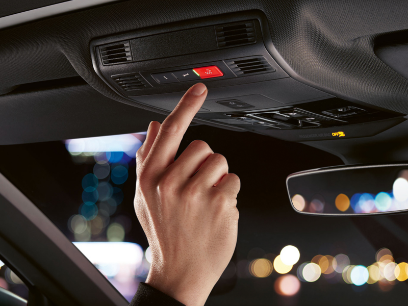 Close-up of a hand pressing red button on interior roof of vehicle.
