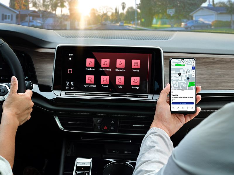 The front passenger in a parked Atlas holds a smartphone in front of the center touchscreen display.