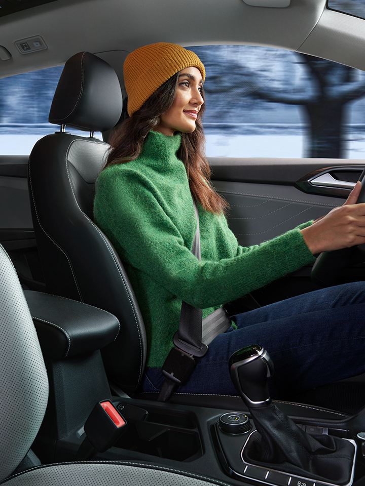 A woman wearing a knit hat and jacket drives a Taos in a snowy landscape.