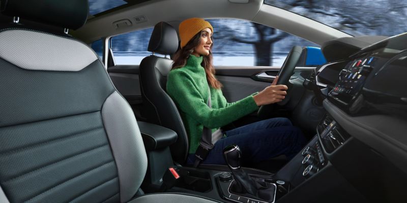 A woman wearing a knit hat and jacket drives a Taos in a snowy landscape.