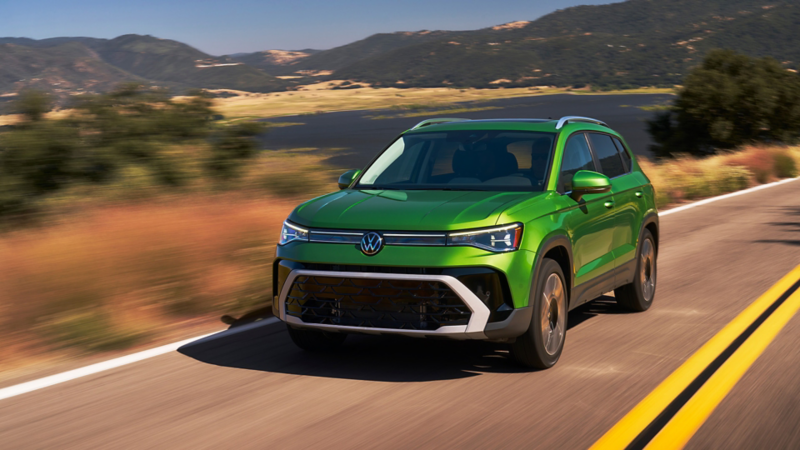Front 3/4 view of a Taos shown in Bright Moss Green driving with a small lake and mountains in the background.