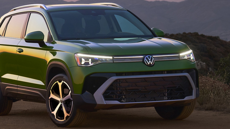 Front 3/4 view of a parked Taos shown in Bright Moss Green at dusk with the LED headlights and available integrated light bar in front grille illuminated with mountains in the background.
