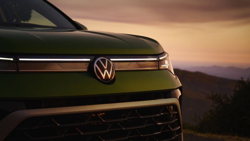 Close up view of a parked Taos shown in Bright Moss Green at dusk with the LED headlights and available integrated light bar in front grille illuminated with mountains in the background.