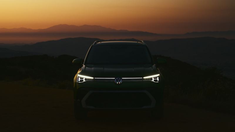 Front of a Taos in Bright Moss Green at dusk with available illuminated grille and front VW emblem.