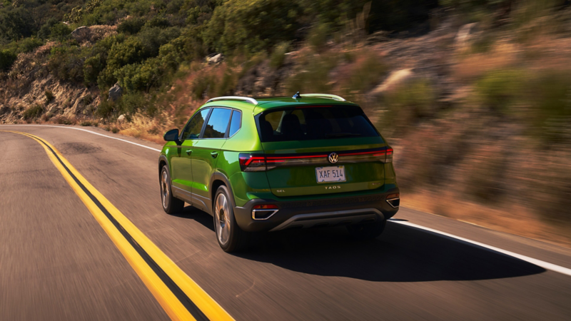 Rear view of a Taos shown in Bright Moss Green driving on a mountain road.
