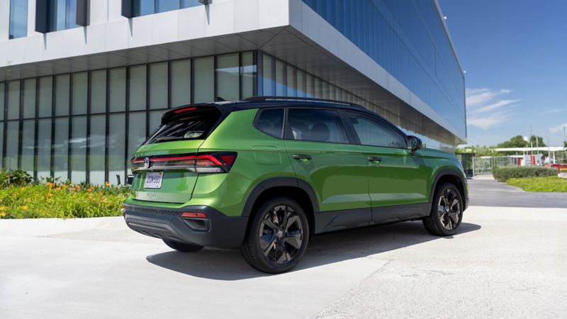 Low rear 3/4 view of a Taos shown in Bright Moss Green parked on in front of a modern architecture building.