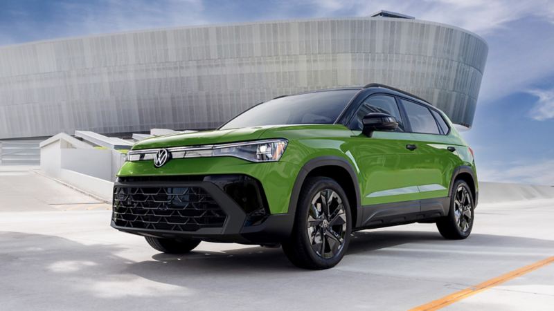 Low front 3/4 view of a Taos shown in Bright Moss Green parked on in front of a modern architecture building.