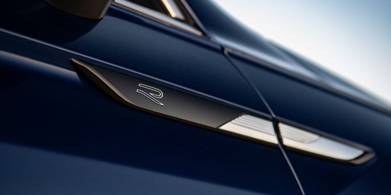 Close up of R-Line badging on door under side view mirror of Tiguan shown in Atlantic Blue Metallic.