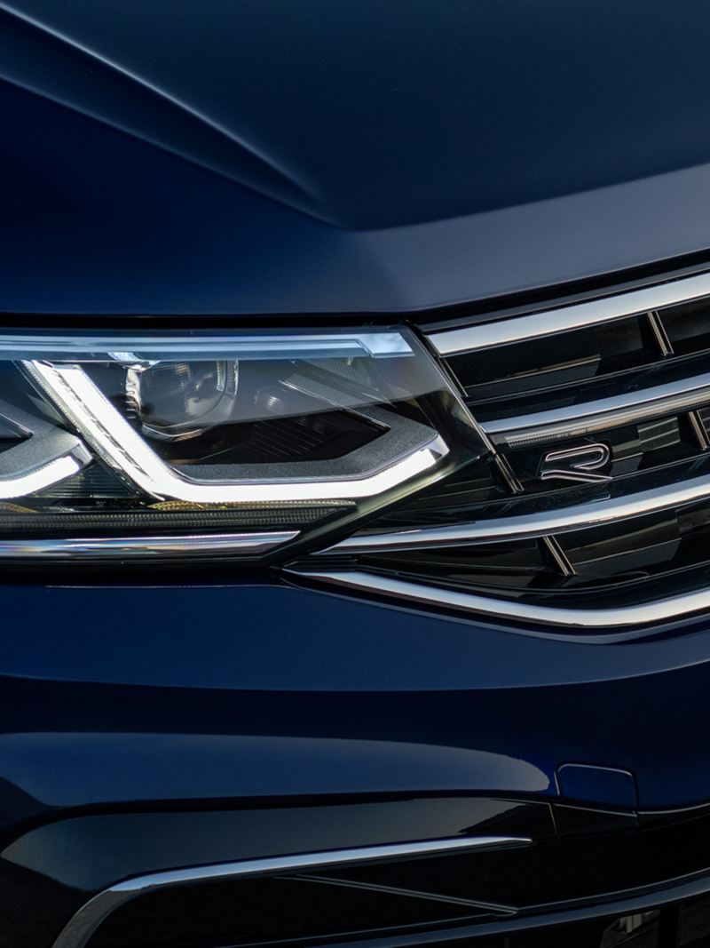 Close up shot of LED headlights and R-Line badge on the front grille of a Tiguan shown in Atlantic Blue Metallic.