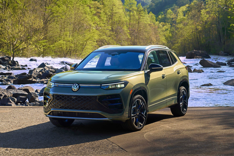 Tiguan shown in Avocado Green  with black roof parked in a front of a river with trees in the background.
