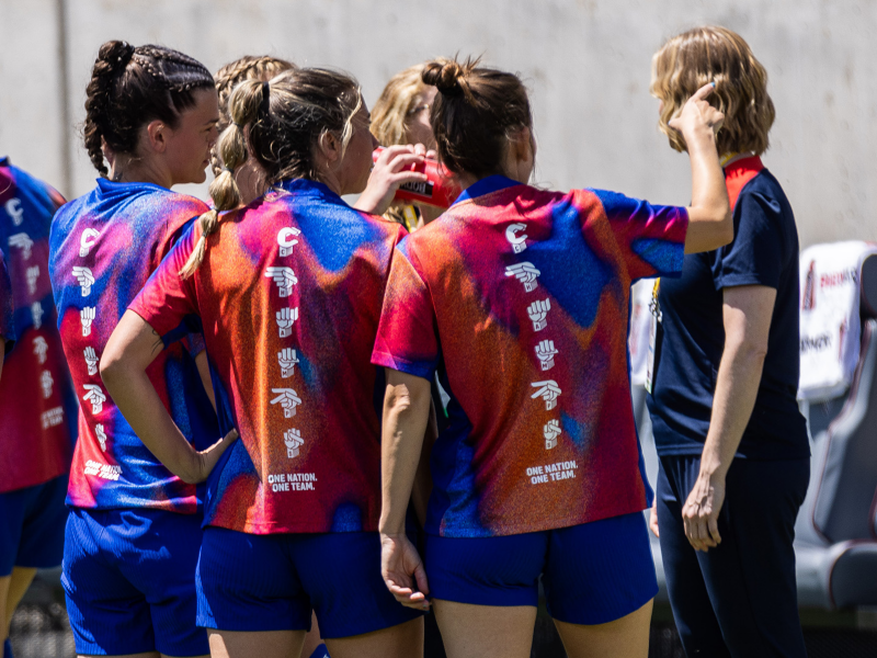 Soccer players stand together and talk while pointing off into the distance.