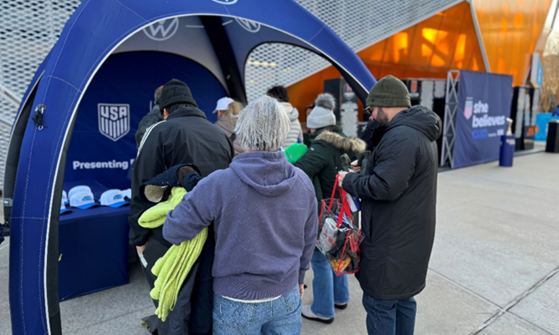 Attendees at a soccer event stand in line at a Volkswagen event booth.