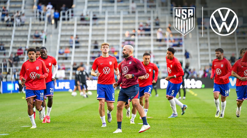 Un equipo de fútbol masculino corriendo por el campo de un estadio mientras se prepara para un partido. 
