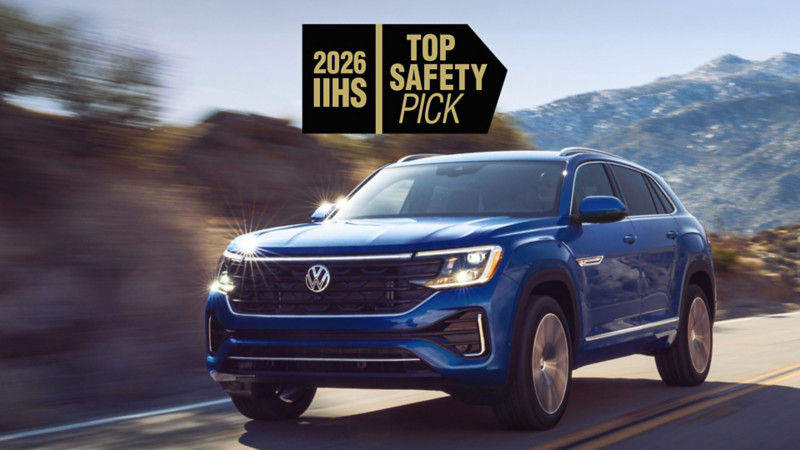 A front view of an Atlas Cross Sport shown in Mountain Lake Blue driving on a wooded mountain road with a safety rating icon overlayed at the top of the image.