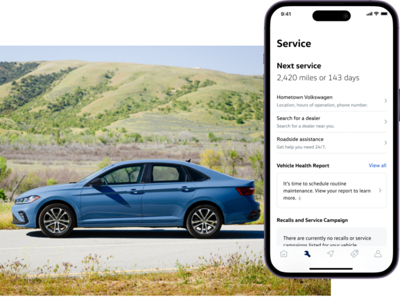 Jetta shown in Monterey Blue Pearl parked with wooded hills in the background. The myVW app is displayed on a superimposed mobile phone. 