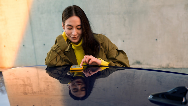 Une femme tapant son téléphone sur le toit d'une Volkswagen, lien vers feedback.vwmodels.ca