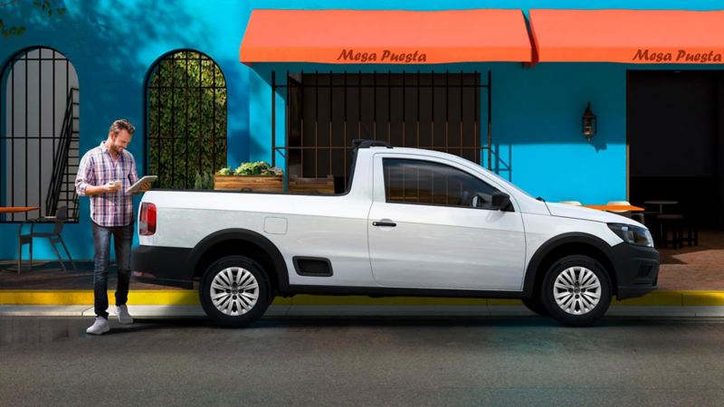 Camioneta pick up - Saveiro 2022 en color blanco cerca de un negocio con un hombre que revisa listado. 