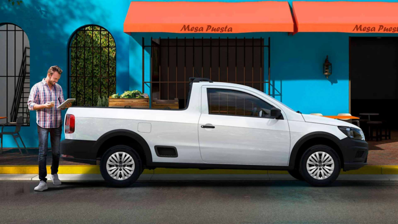 Camioneta en promoción. Volkswagen Saveiro 2022 versión Robust en color blanco, afuera de un restaurante.