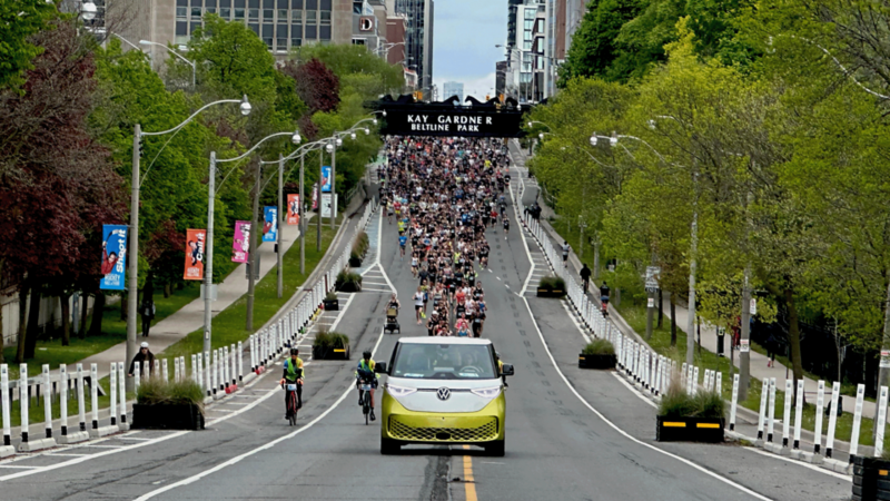 Un ID. Buzz de VW roule devant un grand groupe de coureurs de marathon. 