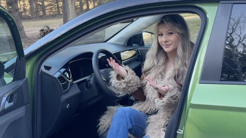 Jessica sitting in the driver’s seat of a green 2025 Taos with the door wide open, smiling at the camera.