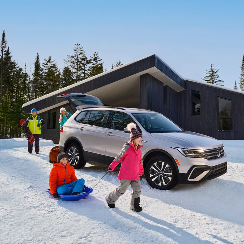 We see two children playing with snow in winter clothes by a grey Volkswagen Tiguan.