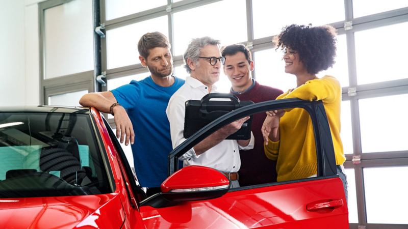 Group of people having a discussion next to a red car