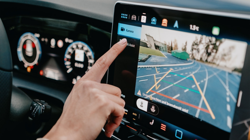 Un doigt touche l'écran dans la Golf, et on voit la vue de la caméra arrière.