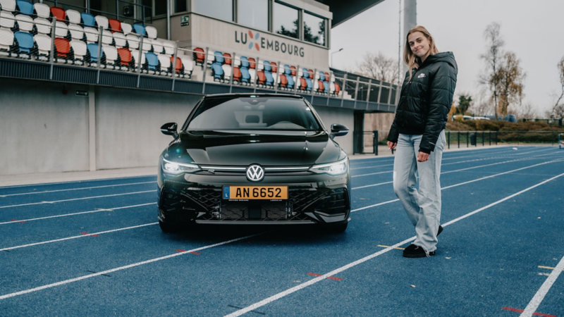 Une femme se tient à côté d'une Golf R-Line noire dans un stade, sur la piste d'athlétisme.