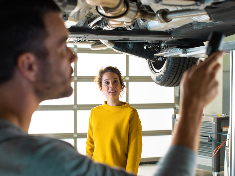Mechanic working on car with woman stood by