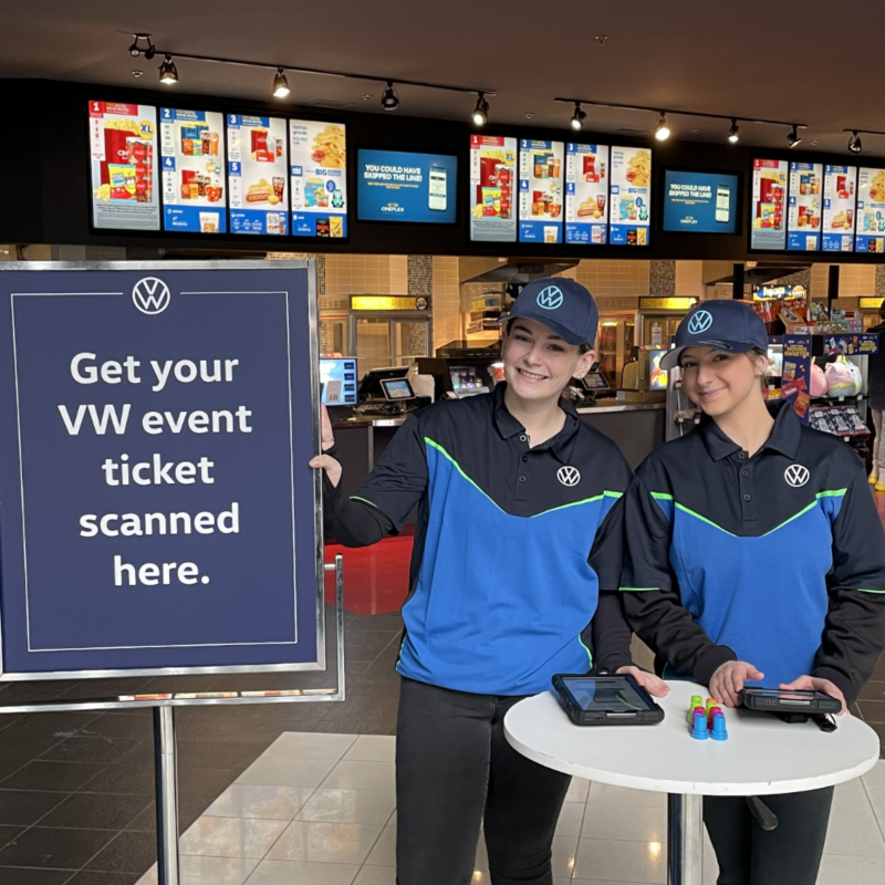 Two VW Brand Ambassadors pose in front of the concession stand at the movie theater as they welcome attendees. 