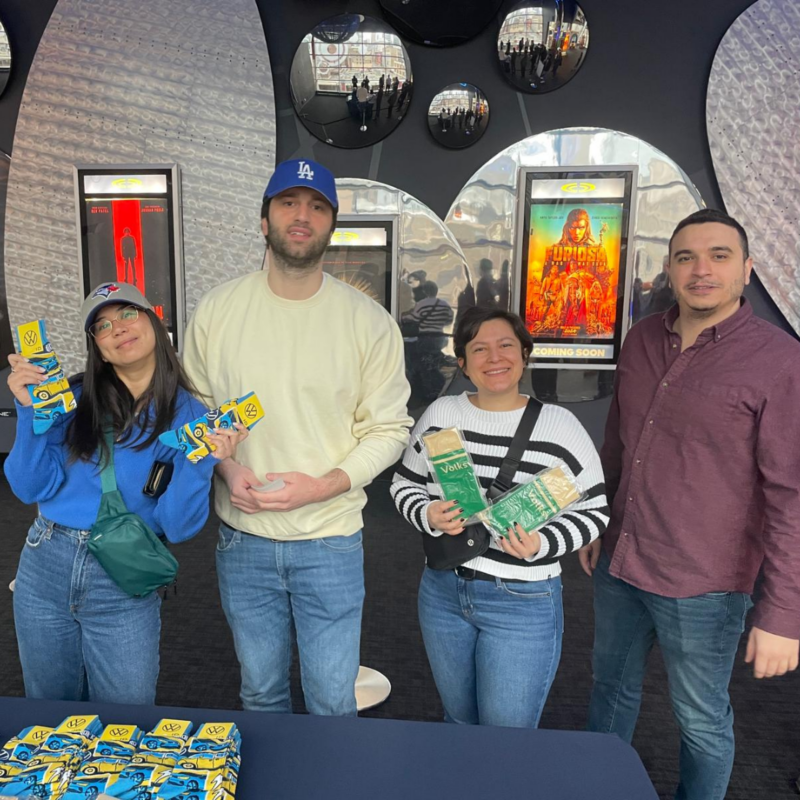 Four people smile for a photo while holding VW-branded socks at the Dune: Part Two movie event. 